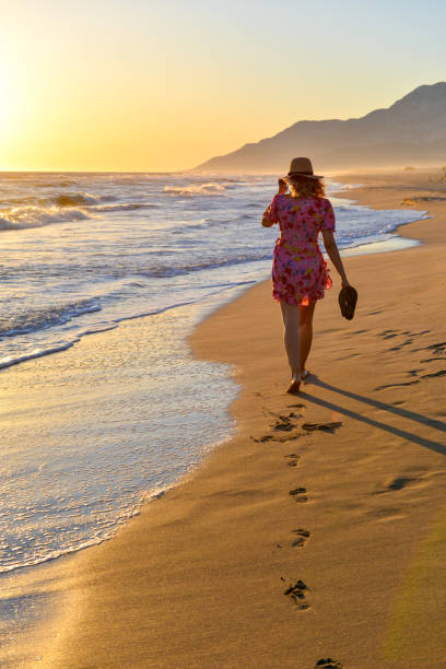 Woman walking on the beach at sunset.