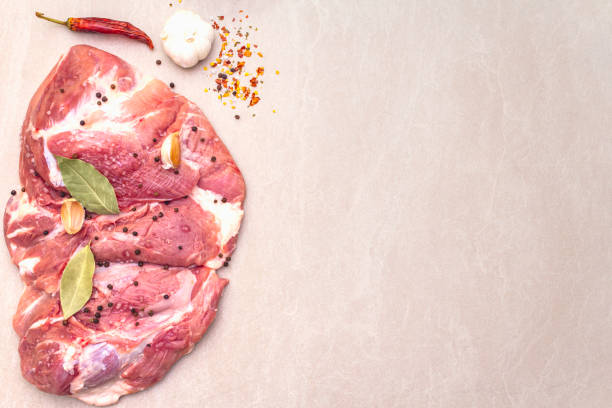 extreme close-up of thinly sliced raw pork, emphasizing its texture on a wooden board with garlic and shallots in the background.