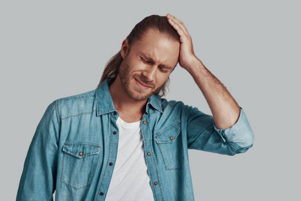 istock So tired. Frustrated young man keeping eyes closed and making a face while standing against grey background 1157130802
