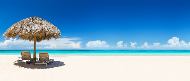 Beach chairs with umbrella and beautiful sand beach in Punta Cana, Dominican Republic. Panorama of tropical beach with white sand and turquoise water. Travel summer holiday background concept.