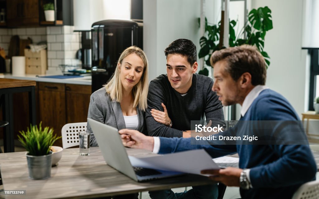Lächelndes Paar mit einem Computer mit ihrem Investmentagenten bei einem Meeting. - Lizenzfrei Rat Stock-Foto Lächelndes Paar mit einem Computer mit ihrem Investmentagenten bei einem Meeting. - Lizenzfrei Rat Stock-Foto