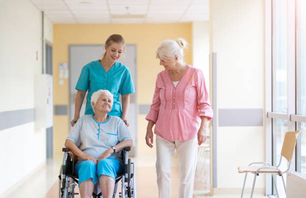 elderly woman on wheelchair with her daughter and nurse - senior adult hospital uniform gray hair imagens e fotografias de stock