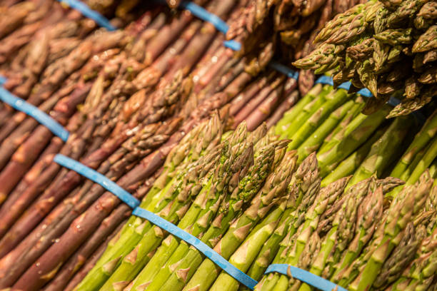 A close up of green and purple asparagus for sale on a market stall