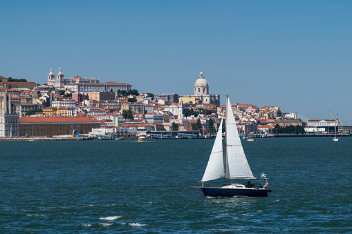Small sailing boat in the Tagus River with the Lisbon skyline on the background; Concept for travel in Portugal and visit Lisbon.