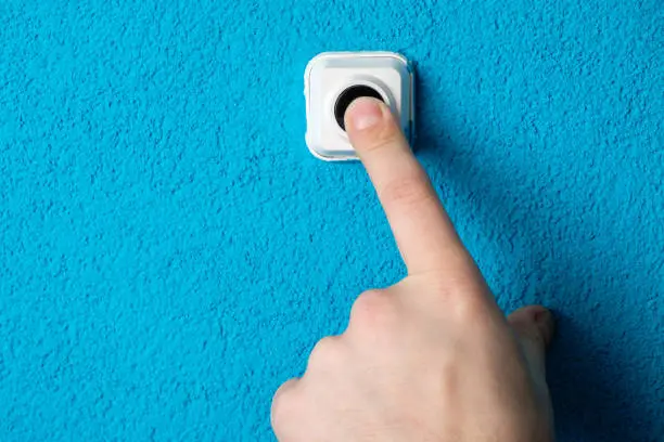 Photo of Close-up of man's hand pressing the button of doorbell on blue wall
