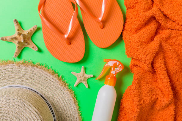istock Summer beach flat lay accessories. Sunscreen bottle cream, straw hat, flip flops, towel and seashells on colored Background. Travel holiday concept with copy space 1157139299