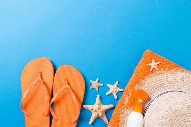 istock Summer beach flat lay accessories. Sunscreen bottle cream, straw hat, flip flops, towel and seashells on colored Background. Travel holiday concept with copy space 1157139481