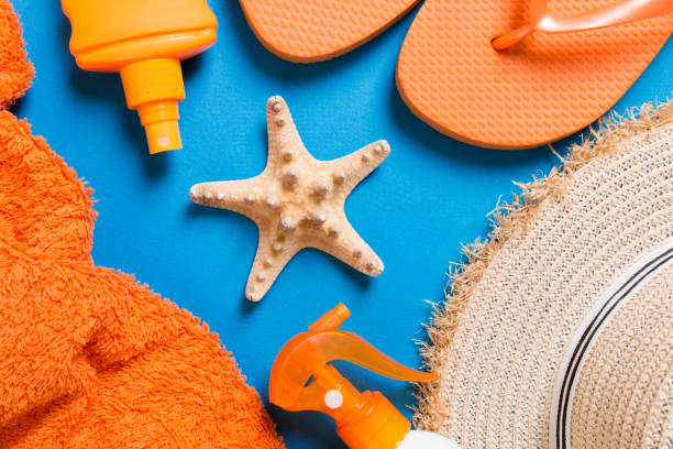 istock Summer beach flat lay accessories. Sunscreen bottle cream, straw hat, flip flops, towel and seashells on colored Background. Travel holiday concept with copy space 1157139558