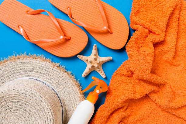 istock Summer beach flat lay accessories. Sunscreen bottle cream, straw hat, flip flops, towel and seashells on colored Background. Travel holiday concept with copy space 1157139596