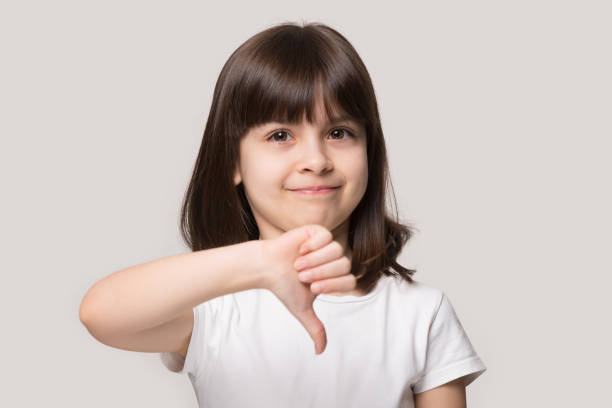 istock Little girl looking at camera showing thumb down studio shot 1157139758