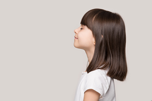 Profile side view face brown-haired little girl standing isolated on beige studio background, preschool kid do deep breath enjoy fresh air or dreaming fill with energy feeling healthy and good concept