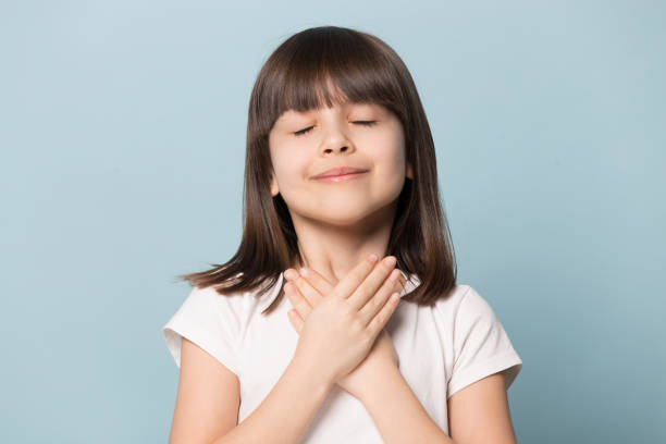 grateful little girl closed eyes hold hand on chest - praying girl imagens e fotografias de stock