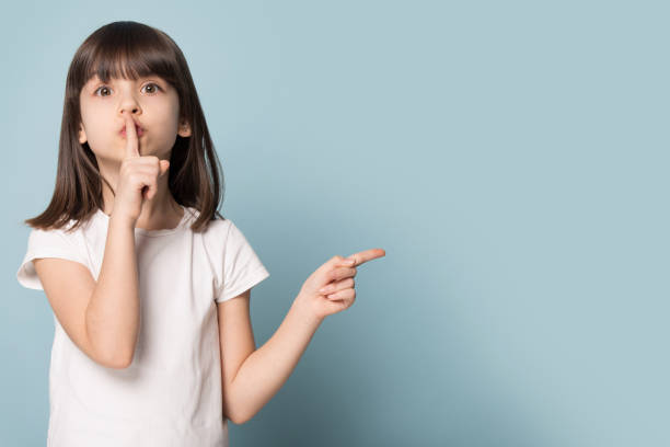 Funny little girl hold finger on lips pointing on copyspace Adorable six years old little girl holding finger on lips symbol of hush gesture of asking to be quiet. Silence or secret concept image isolated on blue studio background with copy free space for text finger on lips stock pictures, royalty-free photos & images