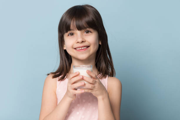 petite fille retenant le verre avec la pose de lait d'isolement sur le bleu - milk child drinking little girls photos et images de collection