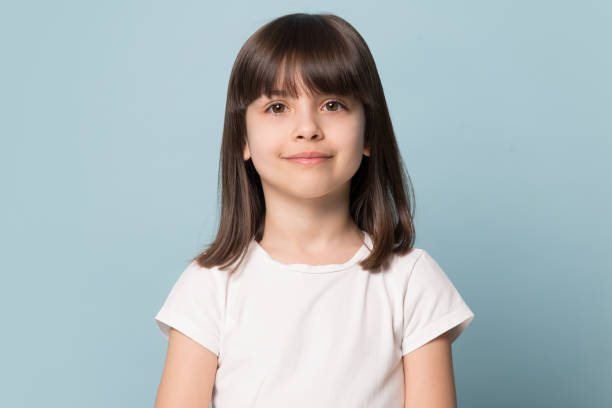 Little girl looking at camera isolated on blue studio background Adorable six years old girl in white t-shirt isolated on blue studio background, pretty brown-haired fringe hairstyle european appearance child pose indoor smiling look at camera, generation Z concept 6 7 years stock pictures, royalty-free photos & images