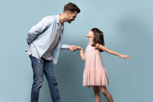 Father and little daughter holding hands dancing waltz studio shot Elder brother younger sister dancing waltz enjoy time together, loving young father gentleman and little daughter princess in pink dress standing holding hands family pose isolated on blue background dancing dad stock pictures, royalty-free photos & images