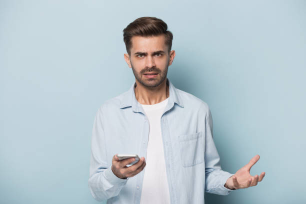 istock Angry man holding smart phone looking at camera studio shot 1157139795