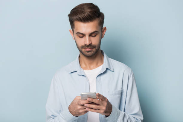 istock Serious guy holding smartphone standing isolated on blue studio background 1157139799