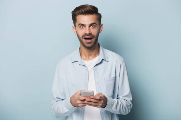istock Man looking at camera holding smartphone feeling amazement 1157139801