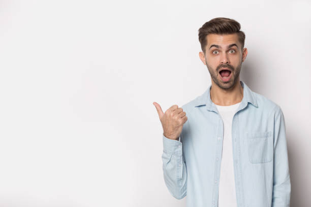 Guy opened mouth gawp at camera pointing finger at copyspace Millennial guy in casual clothes gawp look at camera with opened mouth feels stunned pointing finger at white studio background copy space, advertising services or products, show shocking news concept gawp stock pictures, royalty-free photos & images