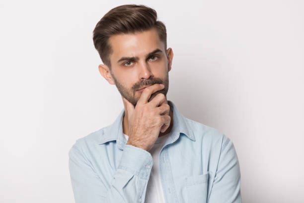 istock Thoughtful young man holding hand on chin feeling doubtful 1157139810