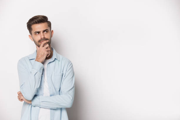 Pensive guy feeling doubtful pose isolated on white studio background Thoughtful man holding hand on chin pose of indecision, look aside at copy space isolated on white grey studio background considering making difficult feeling doubtful about on freespace text concept skeptical look stock pictures, royalty-free photos & images