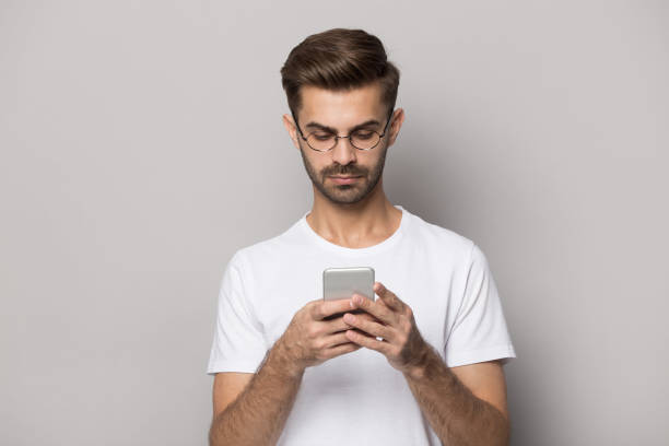 istock Serious guy holding cellphone standing isolated on grey studio background 1157139834
