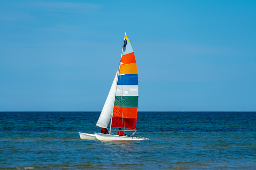 catamaran sailing boat with a very colourful sail with 7 different colours