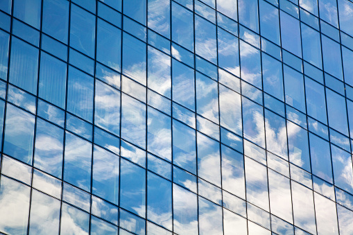 Glass mirror skyscraper wall with blue sky and white clouds reflection close up, modern business center view, financial city district, commercial downtown design, geometric texture pattern, copy space