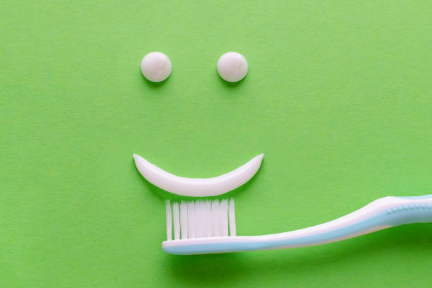a face with smile from white toothpaste, teeth care concept, toothbrush on green background, flatlay