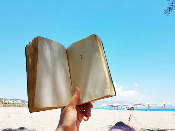 istock young man  lies on the beach reading a book 1157143837