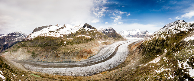 Aerial drone video of the scenic Aletsch Glacier (Aletschgletscher) in the Swiss Alps. The glacier and the surrounding areas are on the UNESCO World Heritage list. Unfortunately with climate change the glacier has been melting as global warming gets worse through the greenhouse effect caused by carbon dioxide emissions. The surrounding mountain peaks are snow capped.