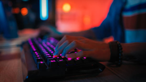 istock Close Up Hands Shot Showing a Gamer Pushing the Keyboard Buttons while Playing an Online Video Game. Keyboard Led Lights. Gamer is Wearing a Bracelet. Room is Dark. 1157159062