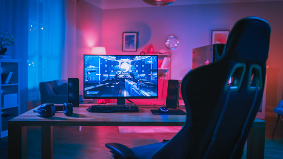 Potente juego de ordenador personal Rig con juego de disparos en primera persona en la pantalla. Monitor se encuentra sobre la mesa en casa. Habitación acogedora con diseño moderno y lámpara de neón rosa. photo