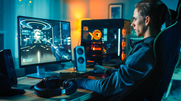 wesoły gracz gra first-person shooter online gry wideo na jego potężny komputer osobisty. pokój i komputer mają kolorowe neonowe diody led. przytulny wieczór w domu. - pc game zdjęcia i obrazy z banku zdjęć