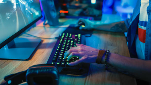 istock Close-Up Hands Shot Showing a Gamer Using the Keyboard while Playing an Online Shooter Video Game. Keyboard has Green Neon Lights in Buttons. Gamer is Wearing a Bracelet. Room is Dark. 1157160004