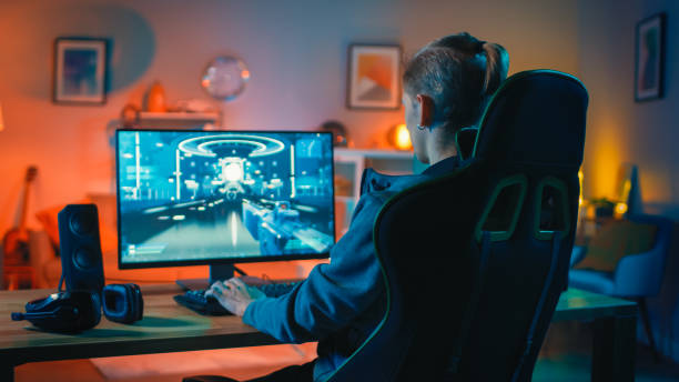 back shot of a gamer playing first-person shooter online video game on his powerful personal computer. room and pc have colorful neon led lights. cozy evening at home. - have imagens e fotografias de stock