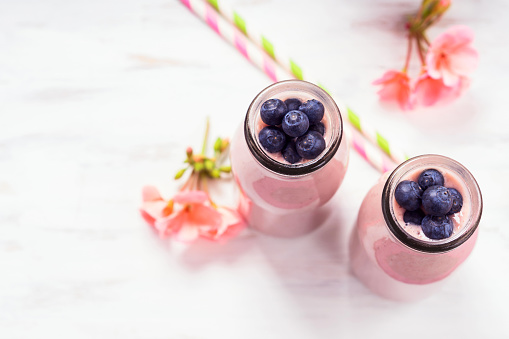 Strawberry banana smoothie topped with blueberries on pink background.