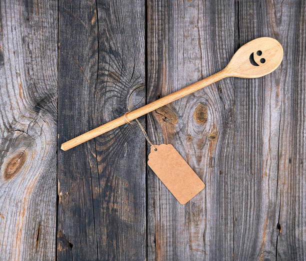 istock wooden spoon with embedded eyes and a smile, empty brown paper tag is attached to the handle with a rope 1157169542