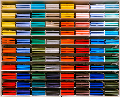 Colorful rainbow clothes background .Various vibrant color shirts perfectly folded on a shelf in the shop. Colored male clothes displayed in store. T-shirt of different color are neatly stacked in a row on the store shelves. Color palette: blue, red, orange, green, purple brown, pink, yellow, blue, khaki ets.