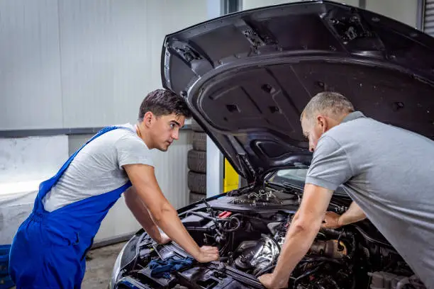 Examining a car. Confident auto mechanic explaining something to a customer while standing near the car. A car mechanic is talking with his mature client. Man mechanic and gray hair man customer discussing repairs done to her vehicle.