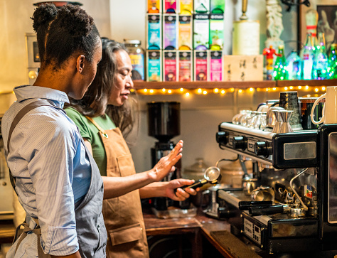 A man showing a new recruit how to make coffee for customers using an espresso machine.