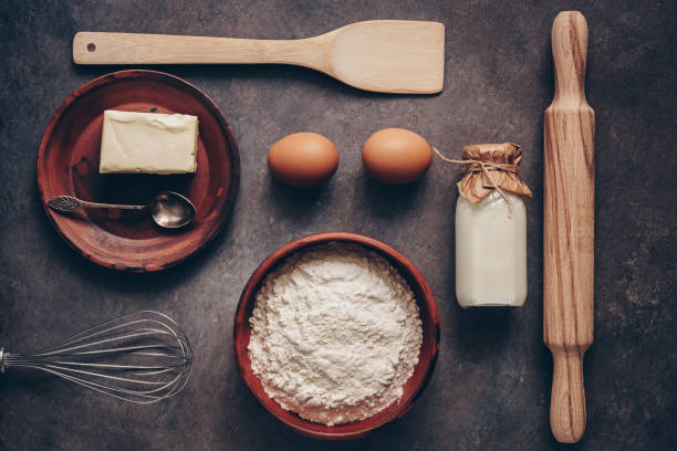 istock Ingredients for baking on a dark rustic background, flour, butter, eggs, rolling pin, whisk and paddle. Top view, flat lay. 1157179101