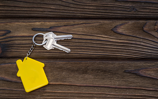 key with yellow shaped house keychain on chain on wood texture background. Idea: buying a house, renting, selling real estate. Mortgage. Loan for housing.