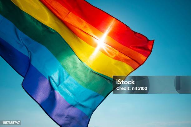 Bandera Arco Iris Ondeando En El Cielo Azul Foto de stock y más banco de imágenes de Bandera del arco iris - Bandera del arco iris, Orgullo, Cultura LGTB