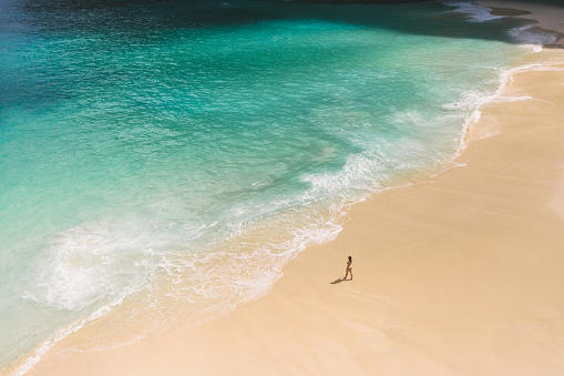 Aerial view of young Caucasian woman walking on scenic beach on Nusa Penida, Indonesia