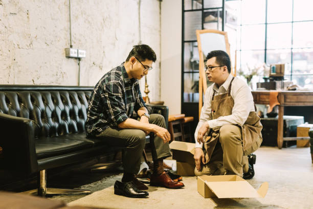 istock Owner looking at customer trying shoes in shop 1157189727