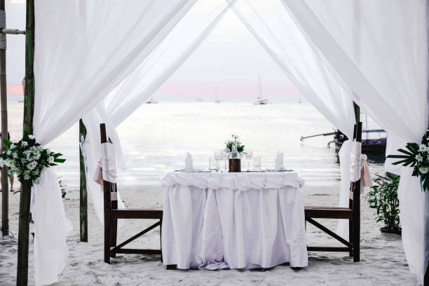 istock White tones. Romantic luxury dinner at tropical beach on sunset. Decorated table with vine on it and chairs 1157191254