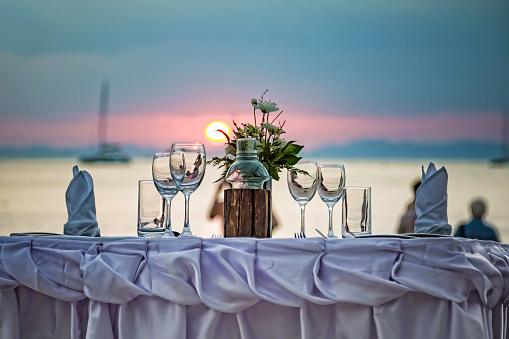 Empty glasses are on the served table. Against the backdrop of a sunset in the sea on a sandy beach