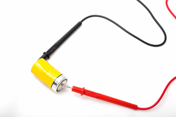 istock Multimeter wires and yellow battery. Checking battery voltage. Red to plus. Close up, isolated on white background 1157191306